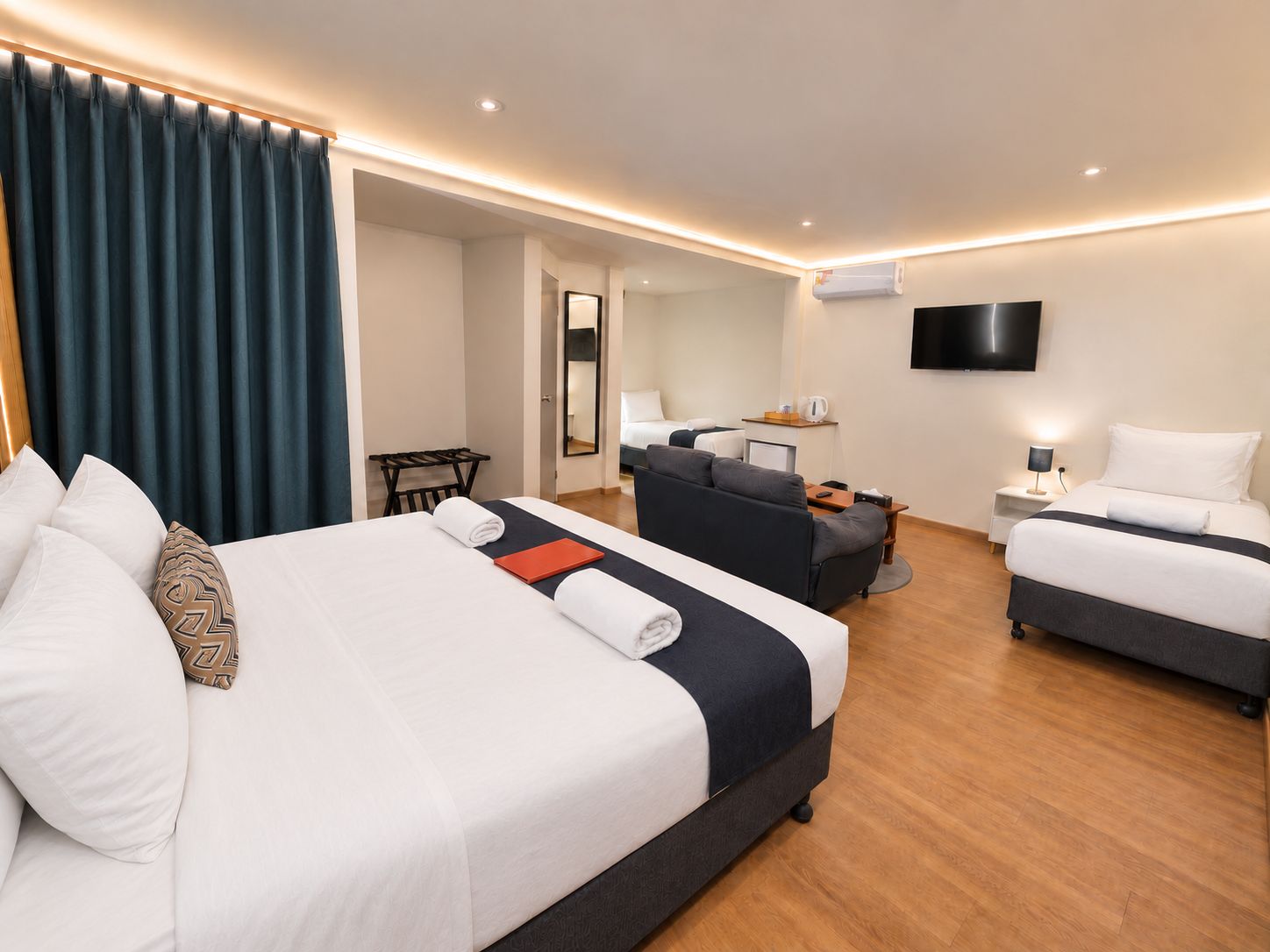 A hotel room with a large bed, a smaller bed, a sofa, a desk, and a TV.