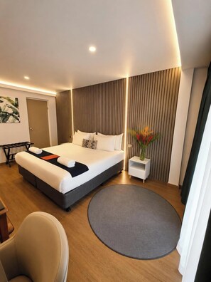 Una habitación de hotel moderna con cama, mesita de noche, silla y alfombra redonda.