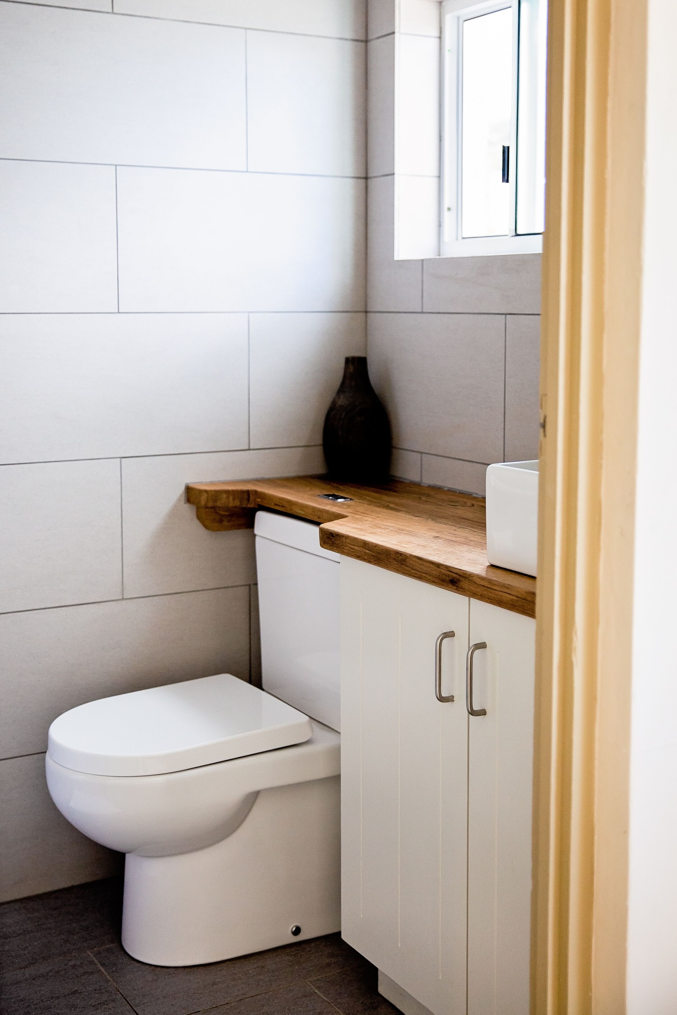 Une salle de bain moderne avec des toilettes blanches, un plan de travail en bois et des meubles blancs.