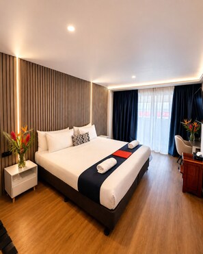 Una habitación de hotel moderna con una cama grande, mesitas de noche, un escritorio y vistas al exterior.