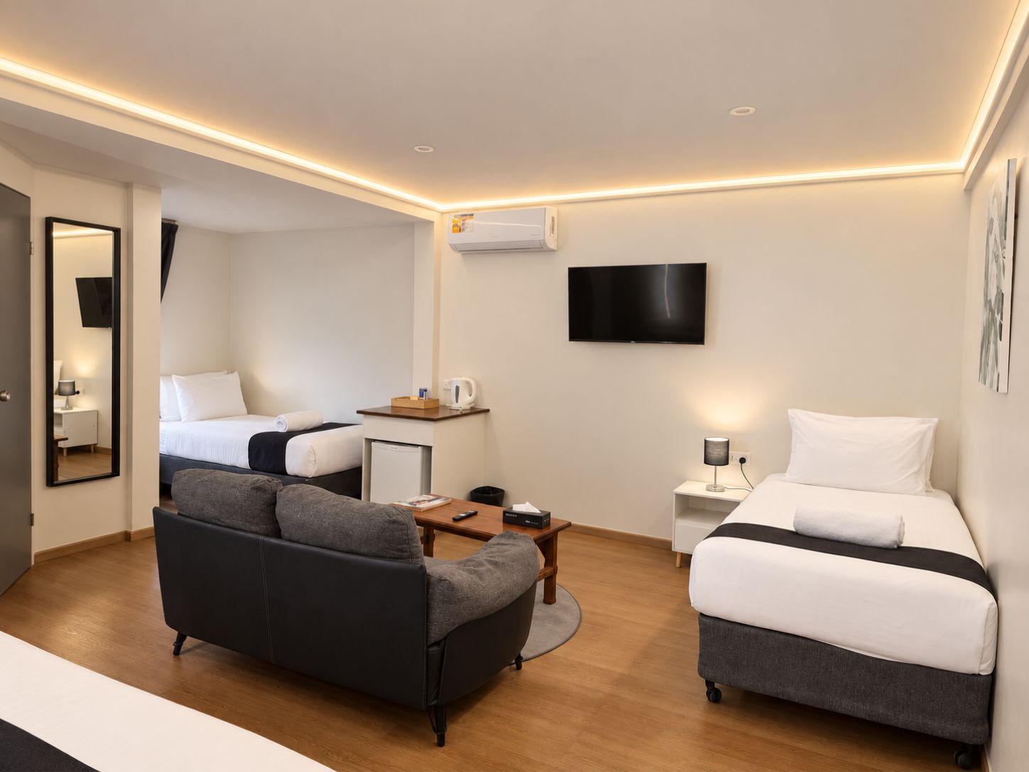 A modern hotel room with a sofa, a bed, a TV, and a small table.