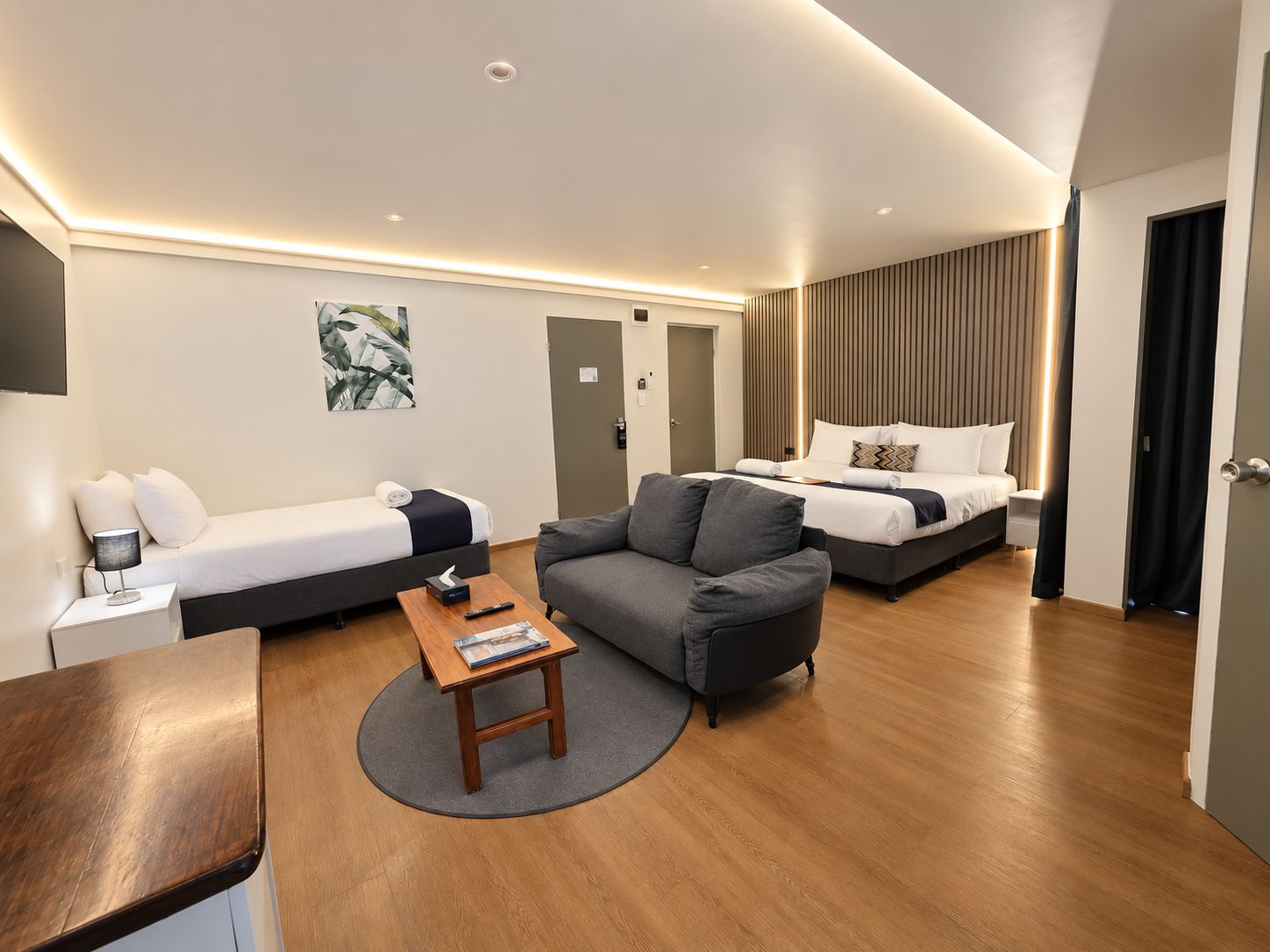 A modern hotel room with a bed, a sofa, a small table, and a TV.