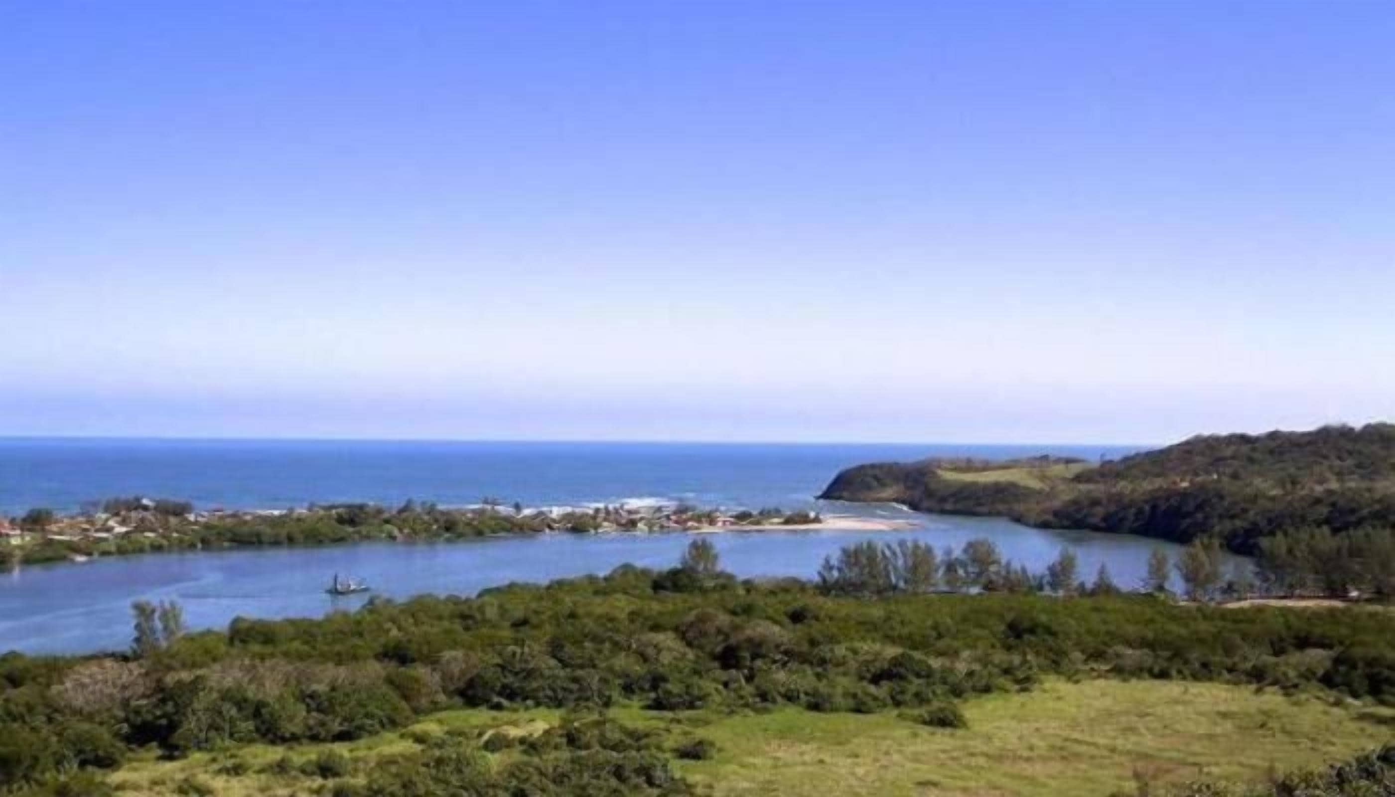 Un paisaje costero con una masa de agua, un pequeño bote y una costa lejana con edificios.