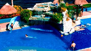 Ein Schwimmbecken mit Wasserfall, Liegestühlen und Reetdachschirmen.