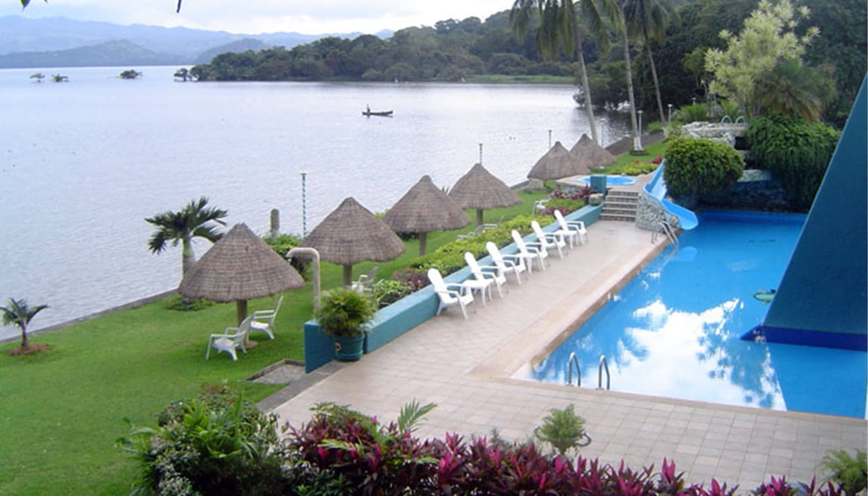 A poolside area with lounge chairs, a water slide, and a view of a lake.