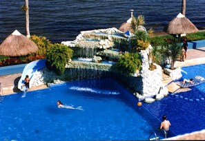 Piscina com cascata, espreguiçadeiras e palmeiras.