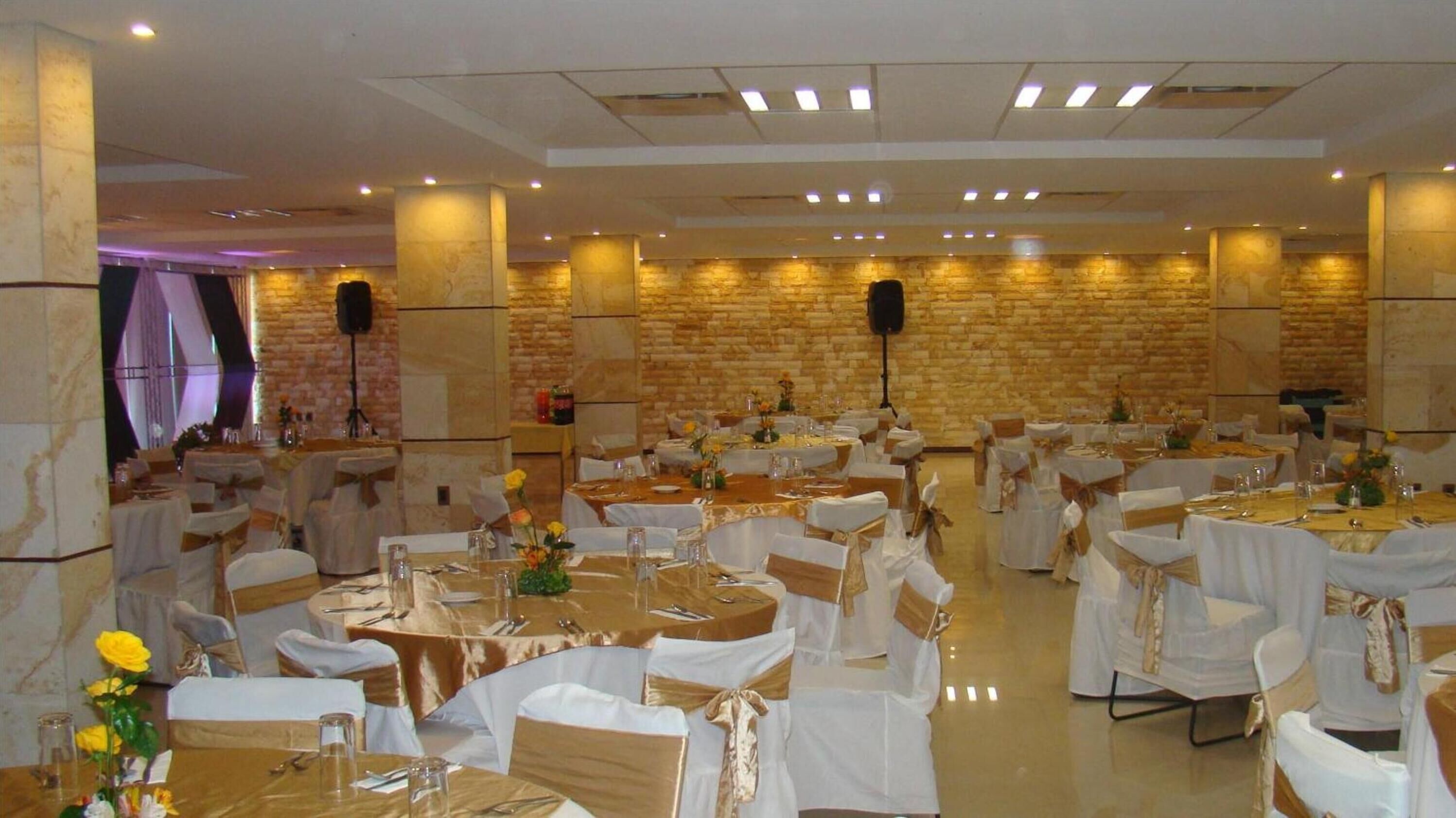A banquet hall with round tables, white tablecloths, and gold sashes.