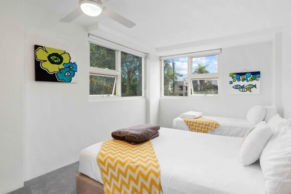 A hotel room with two beds, white walls, and artwork on the walls.