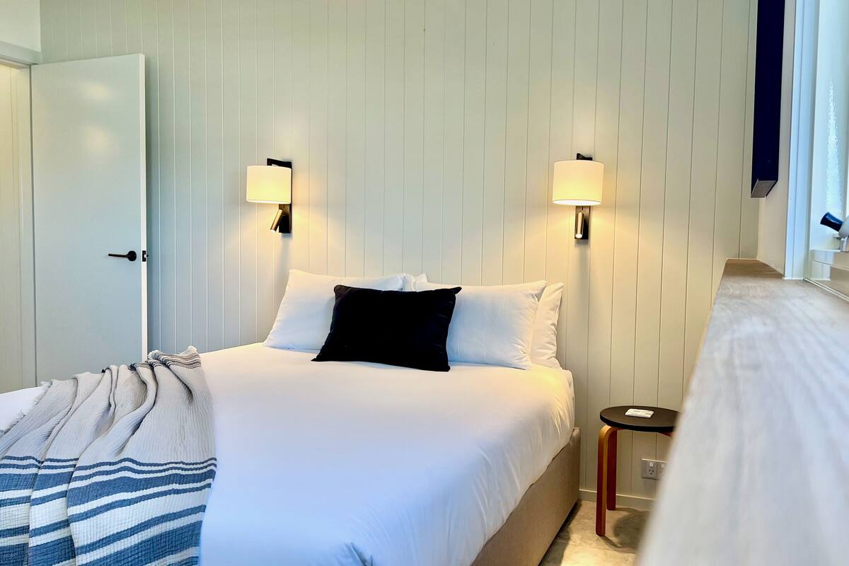 A hotel room with a bed, bedside tables, and wall-mounted lamps.