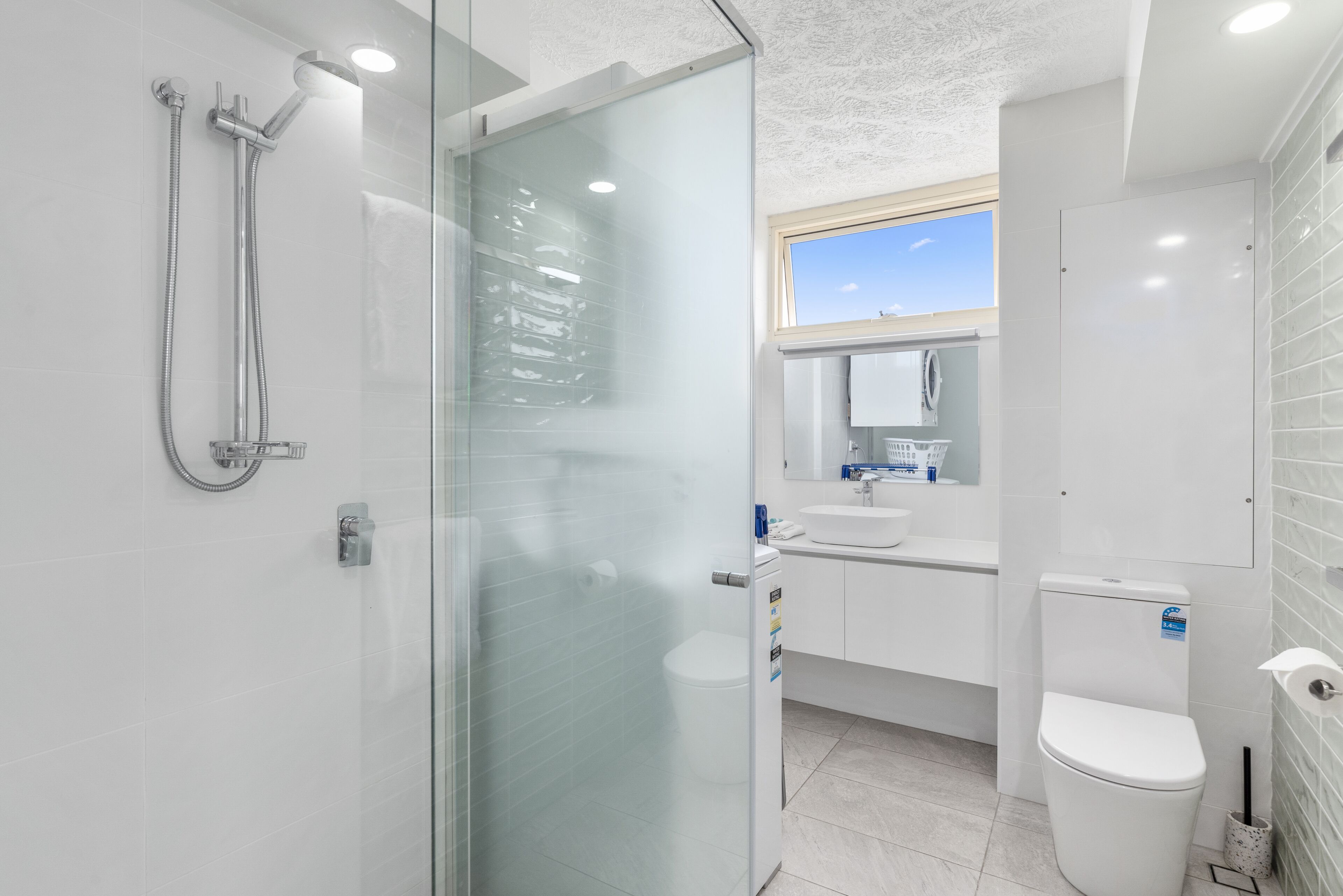 A modern bathroom with a glass shower enclosure, a toilet, and a sink with a mirror above it.