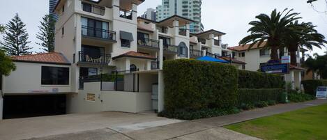 A multi-story residential building with balconies, a garage, and a clear view of a tall building in the background.