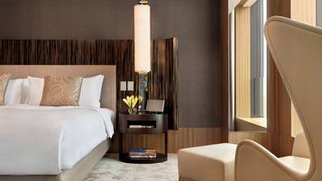 A modern hotel room with a large bed, a bedside table with a lamp, a chair, and a view of the outdoors.