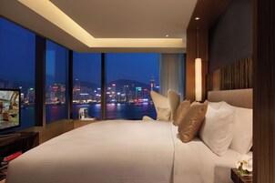 A hotel room with a large bed, a television, and a view of a cityscape at night.
