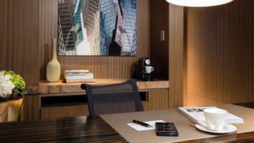 A hotel room with a wooden desk, a coffee machine, a white cup, a smartphone, and a book titled 'A World History of Art'.
