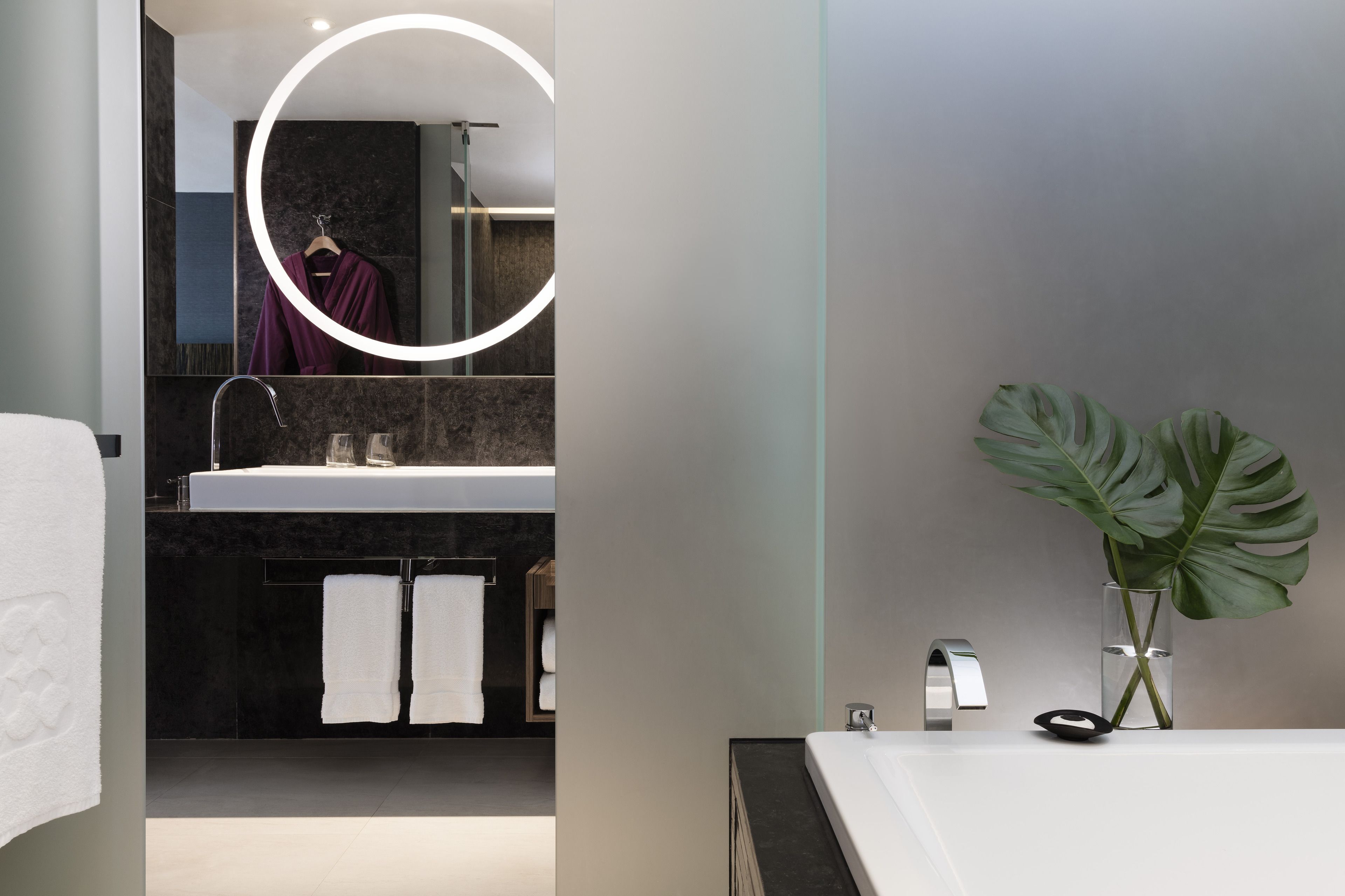 A modern bathroom with a large mirror, a sink, and a potted plant.