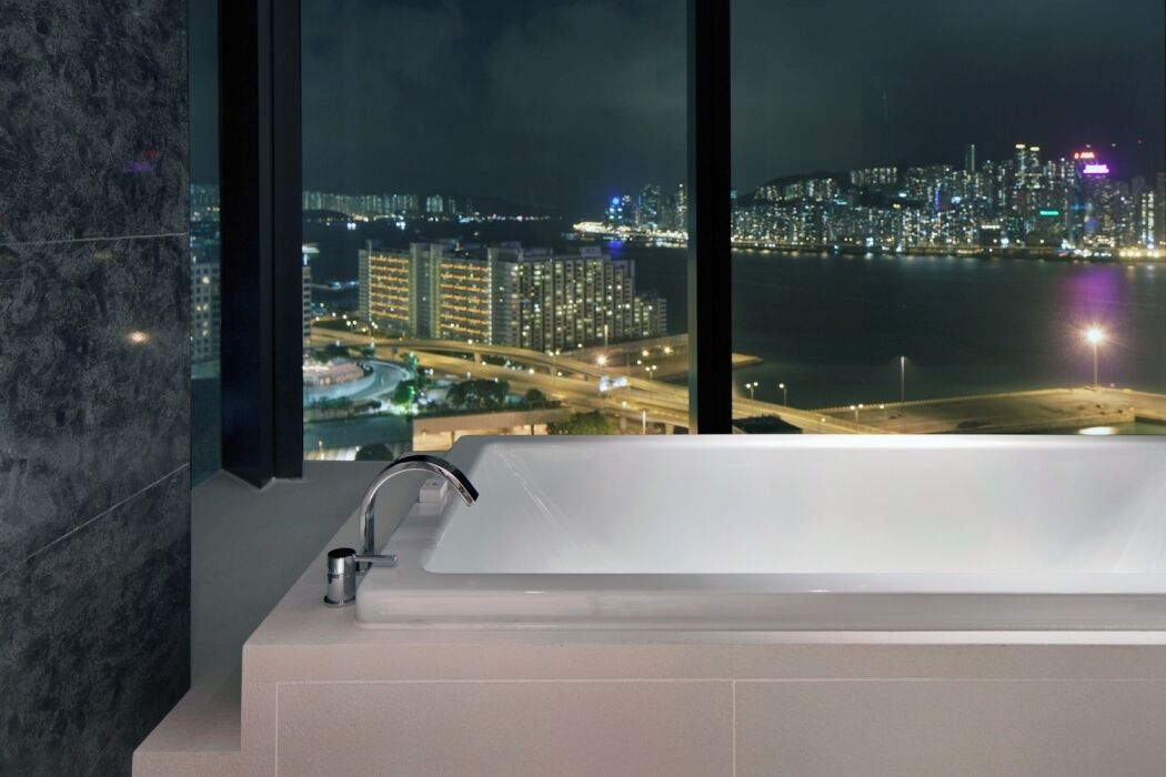 A modern bathroom with a large bathtub, a view of a cityscape at night, and a window with a dark frame.