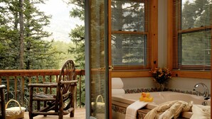 A wooden deck with a wicker chair and a basket, a wooden cabin with a large window, and a bathroom with a bathtub and a flower vase.