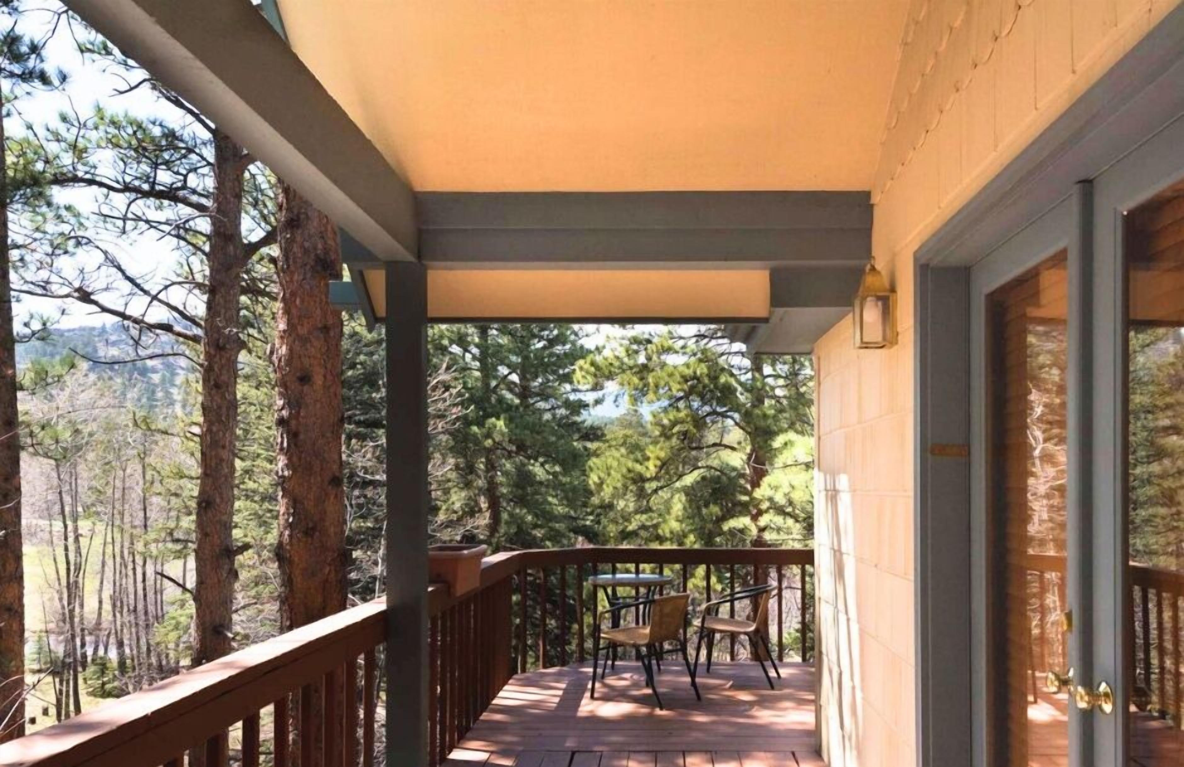A wooden deck with a table and chairs, surrounded by trees and a mountain view.