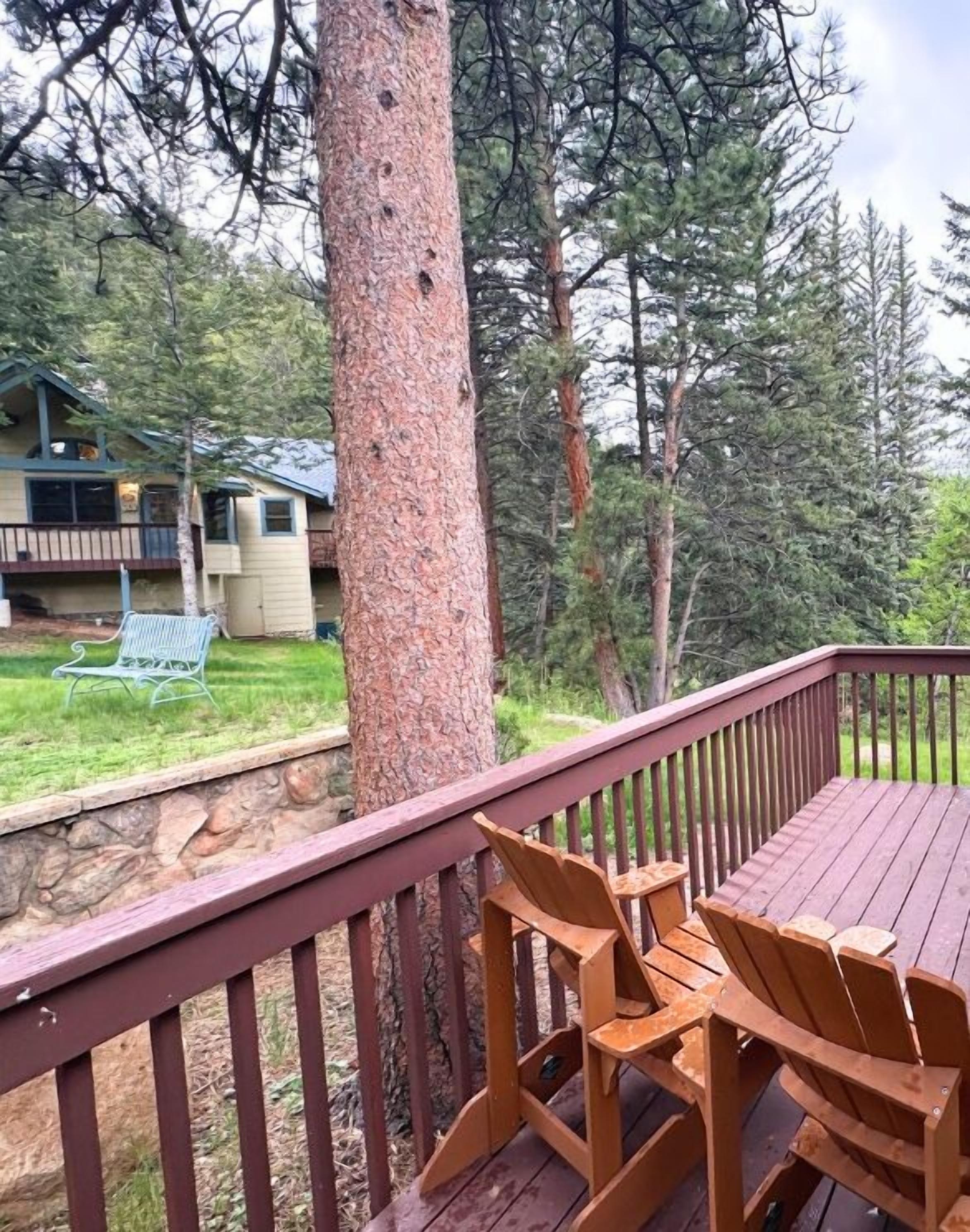 A wooden deck with chairs, a stone wall, and a view of a house and forest.