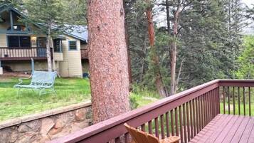 A wooden deck with chairs, a stone wall, and a view of a house and forest.