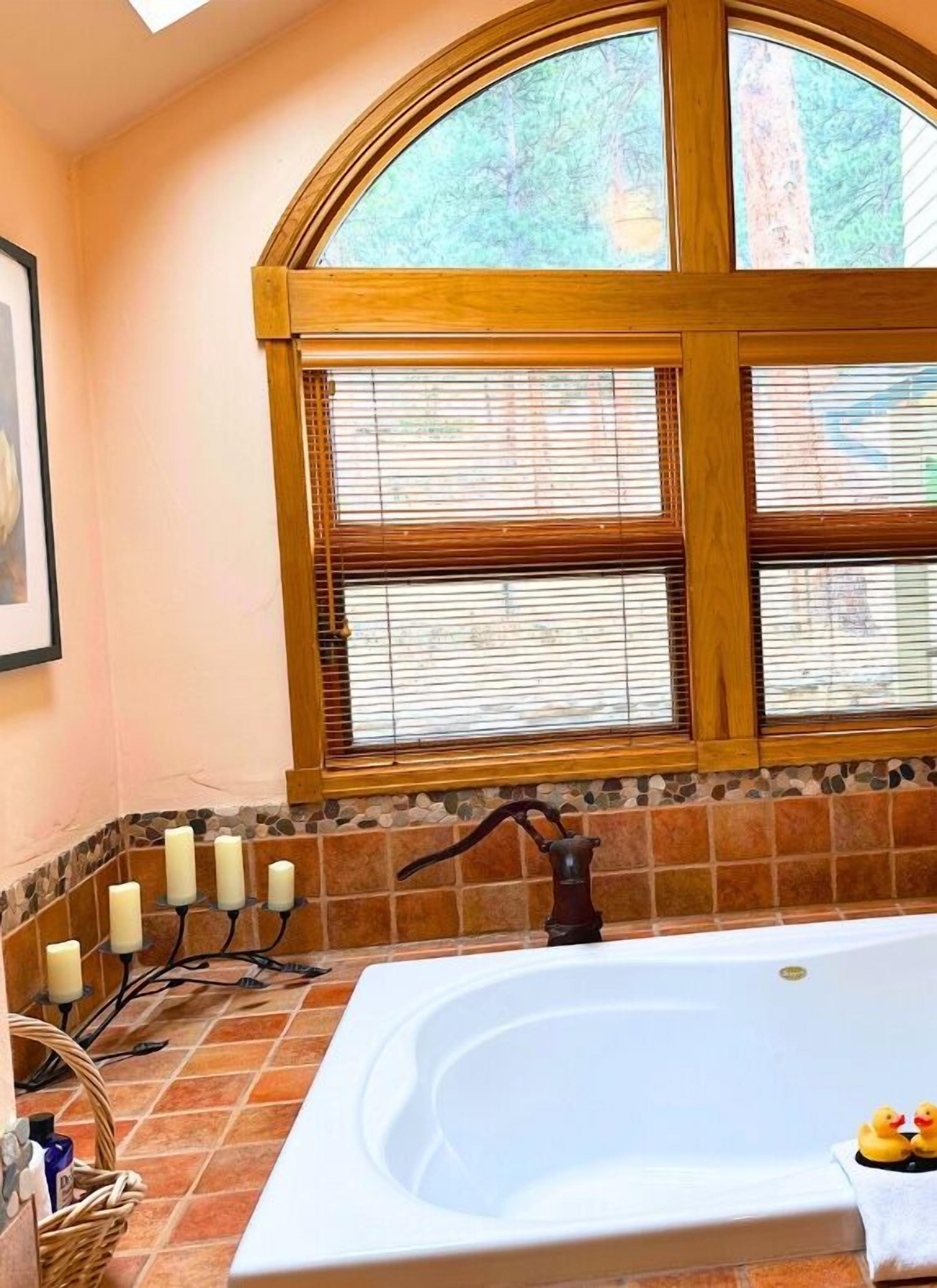 A bathroom with a large bathtub, a wooden window with blinds, and a tiled floor.