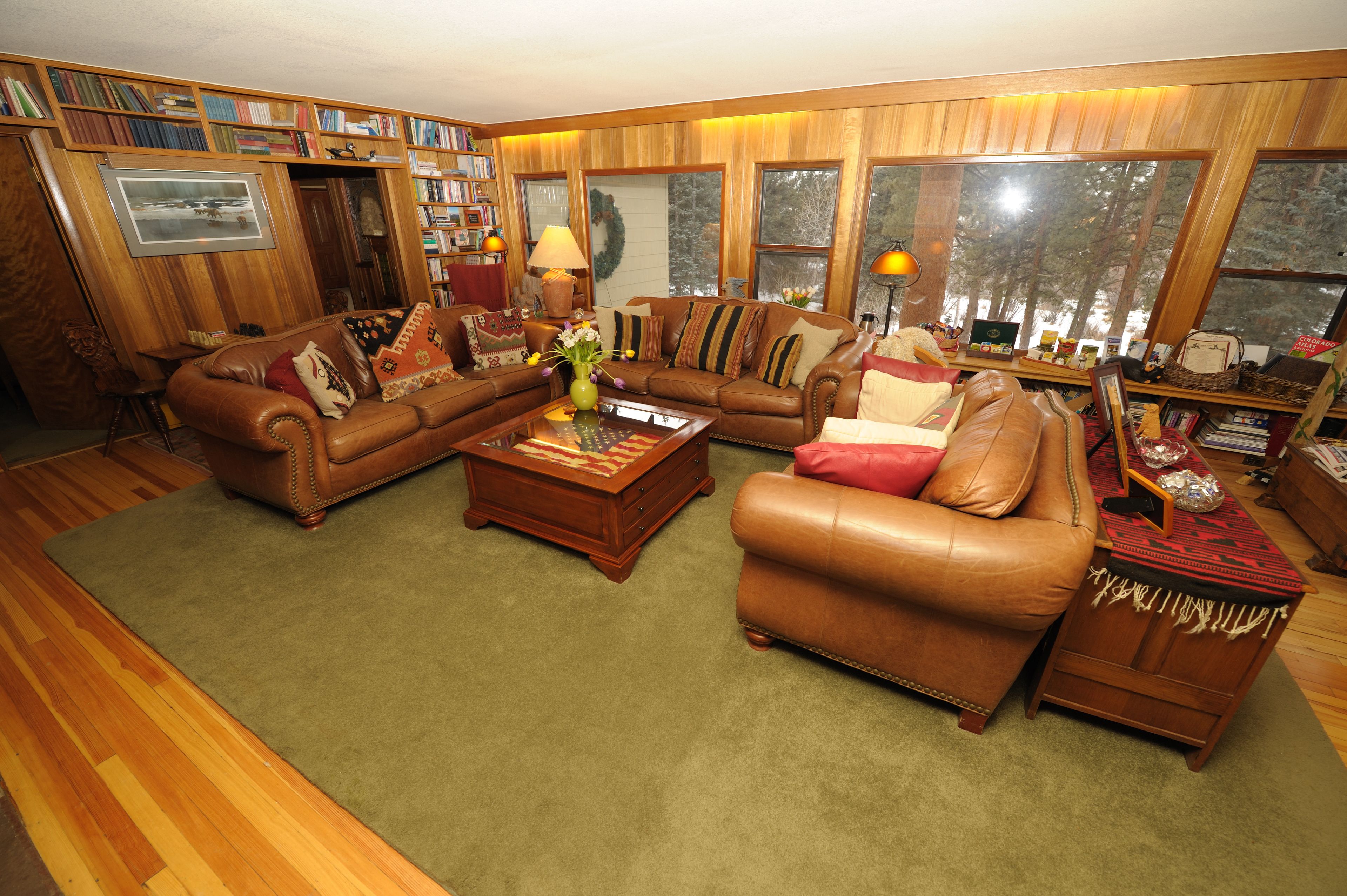 A cozy living room with a brown leather sofa set, a coffee table, and a bookshelf filled with books.
