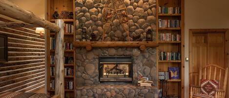 Una habitación acogedora con chimenea de piedra, estanterías de madera y pared de troncos.
