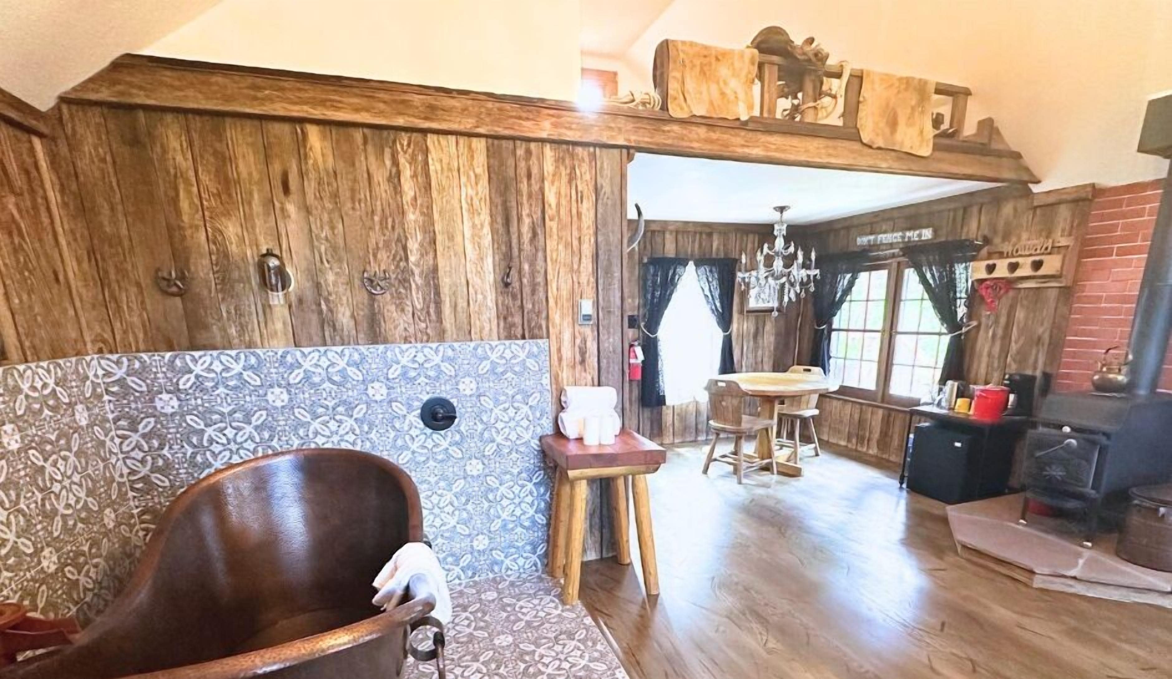 A rustic interior with a wooden chair, a patterned wall, a dining area with stools, and a fireplace.