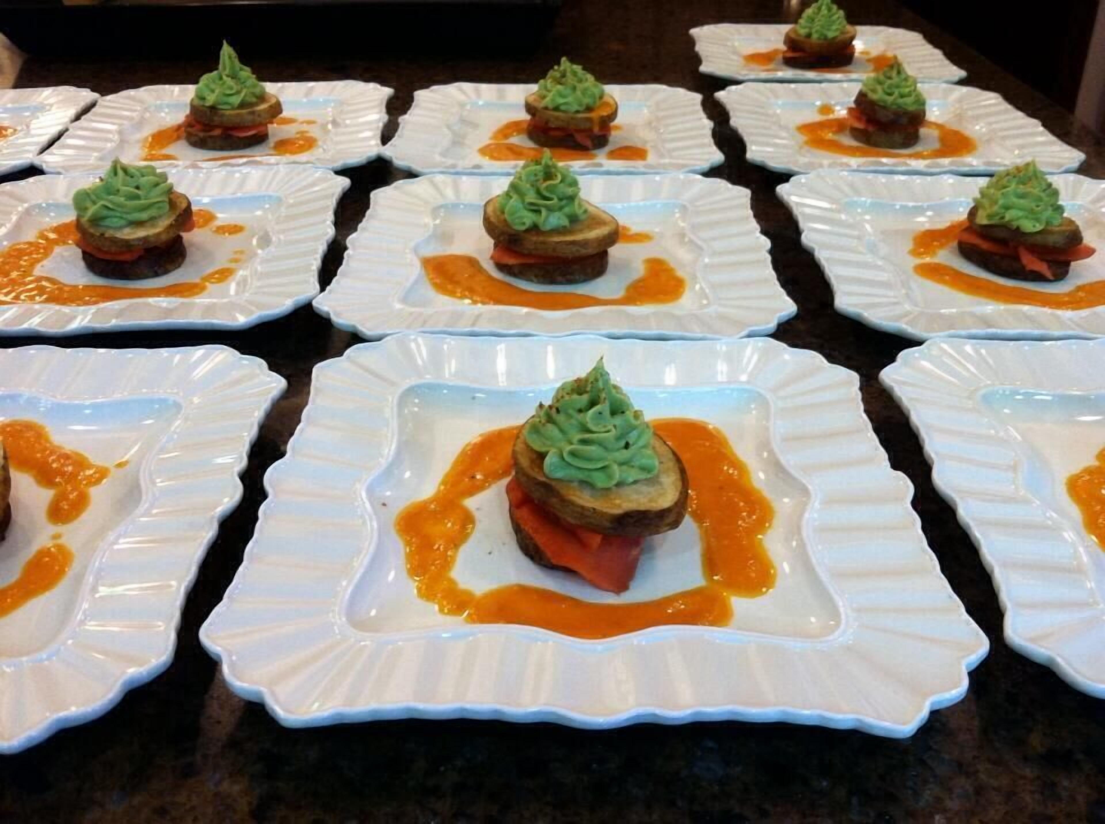 A series of square plates with food items, each topped with a green garnish and surrounded by a sauce.