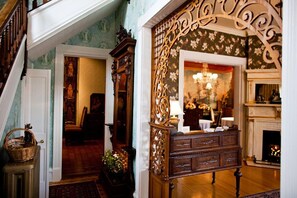 Una gran escalera conduce a una habitación con chimenea, muebles de madera ornamentados y un diseño de papel tapiz floral.