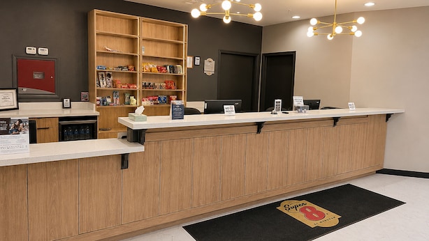 Zona de recepción con mostrador de madera, pantalla digital y estante en la pared con aperitivos.