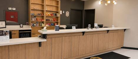A reception area with a wooden counter, a digital display, and a wall-mounted shelf with snacks.