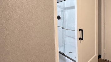 Una puerta que da a un baño con ducha, inodoro y lavabo.
