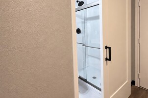 Una puerta que da a un baño con ducha, inodoro y lavabo.