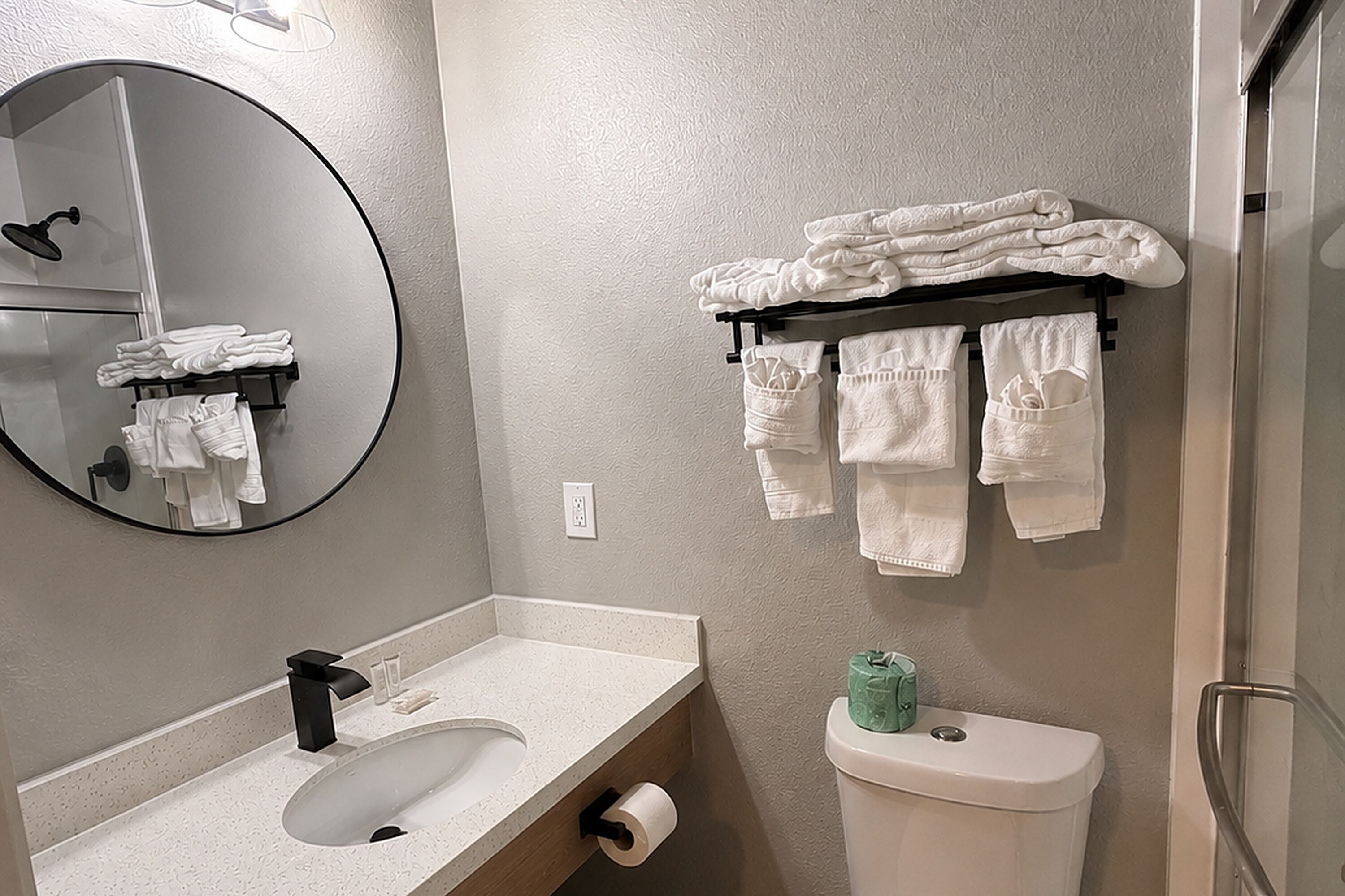 A bathroom with a round mirror, a sink, a toilet, and a towel rack with folded towels.