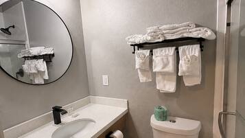 A bathroom with a round mirror, a sink, a toilet, and a towel rack with folded towels.