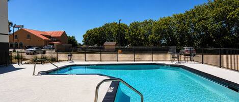 A rectangular swimming pool with a black border and metal handrails, surrounded by a fence and trees.