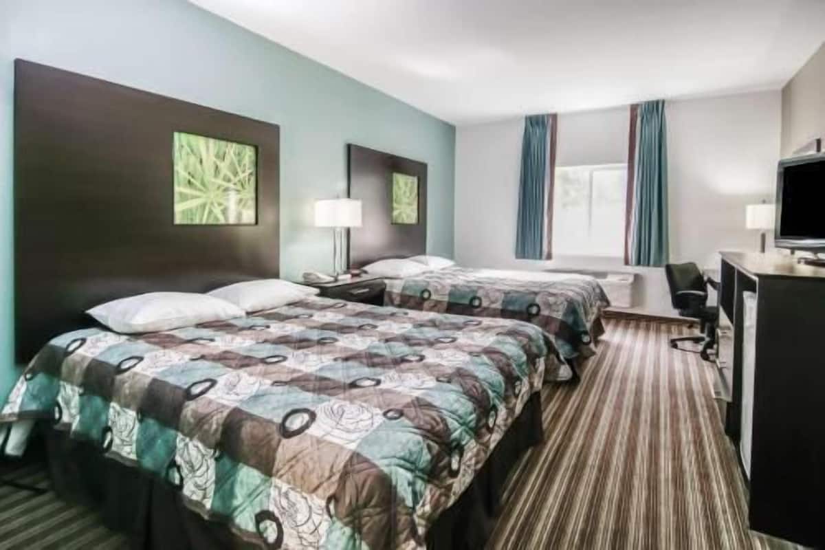 A hotel room with two beds, a desk, a chair, a TV, and a window with curtains.