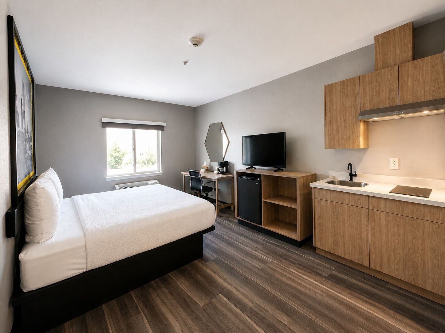 Una habitación de hotel moderna con cama, escritorio, televisor y kitchenette.