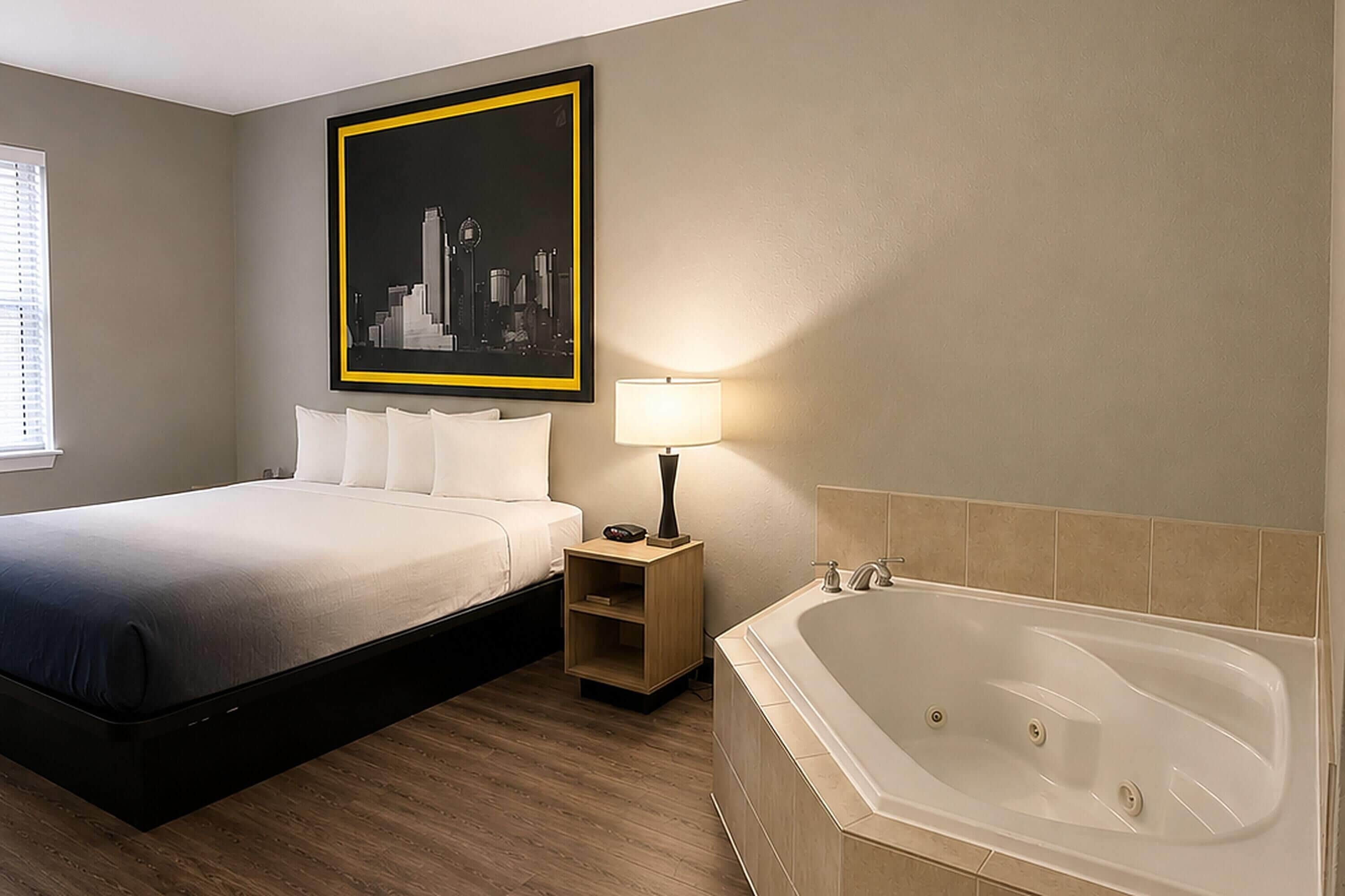 A hotel room with a bed, a nightstand, a lamp, and a bathtub.