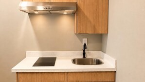 Una cocina con armarios de madera, un lavamanos de acero inoxidable y una placa de inducción negra.