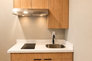 Una cocina con armarios de madera, un lavamanos de acero inoxidable y una placa de inducción negra.