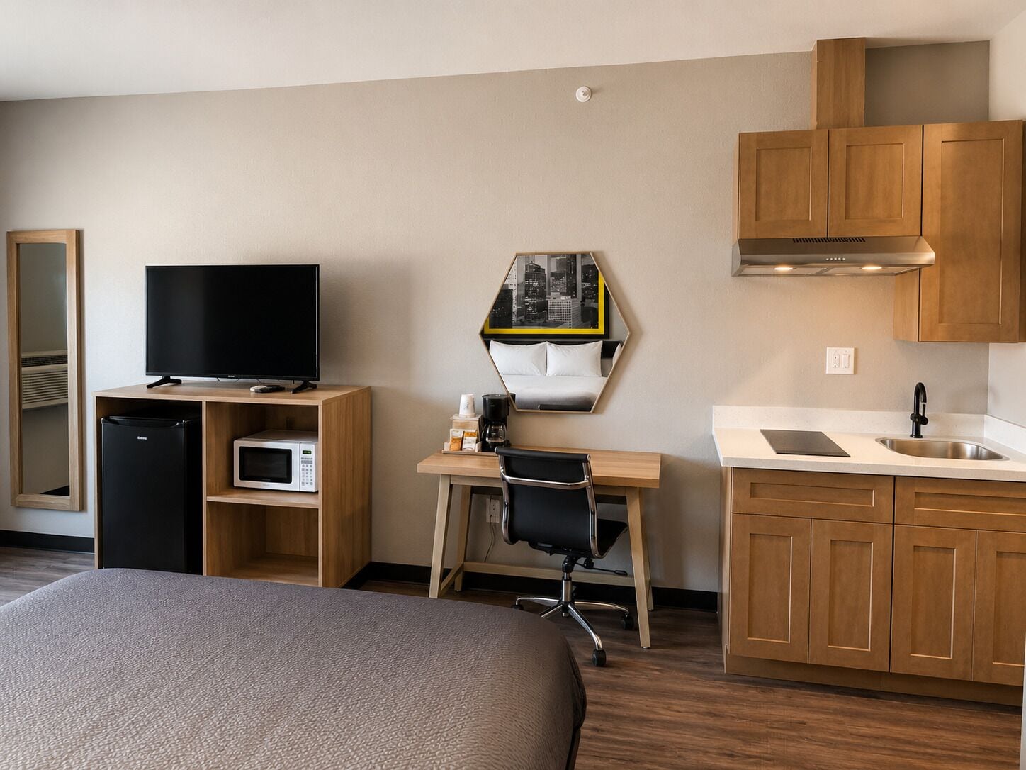 Habitación de hotel con cama, televisión, mini refrigerador, microondas, escritorio con silla, lavamanos y armarios de madera.
