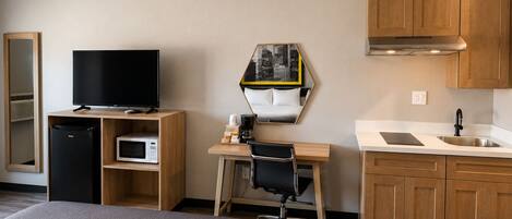 Habitación de hotel con cama, televisión, mini refrigerador, microondas, escritorio con silla, lavamanos y armarios de madera.