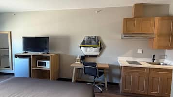 A hotel room with a bed, a desk with a chair, a television, a microwave, a sink, and cabinets.