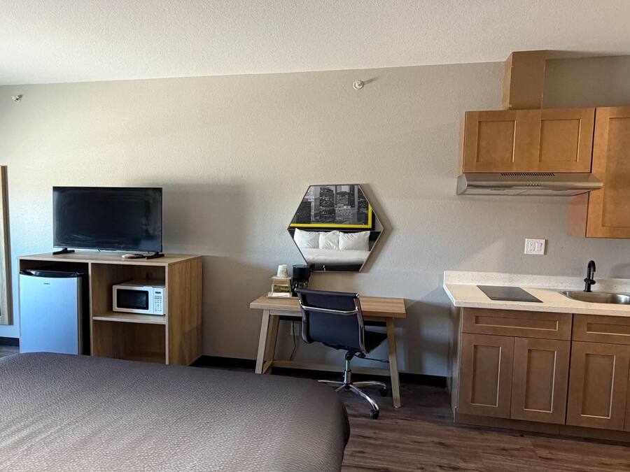 Habitación de hotel con una cama, un escritorio con silla, televisor, microondas, lavamanos y armarios.