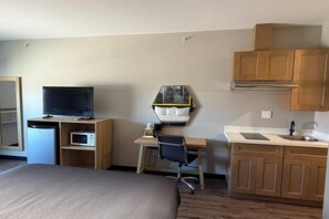 A hotel room with a bed, a desk with a chair, a television, a microwave, a sink, and cabinets. - Super 8 by Wyndham Brenham TX (Brenham)