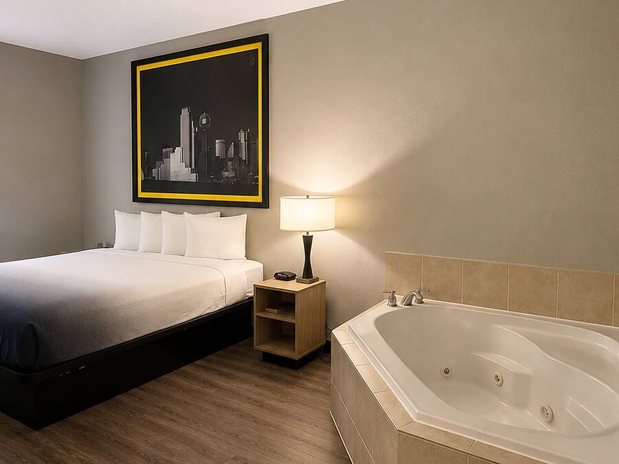 Et hotelværelse med seng, natbord, lampe og badekar.