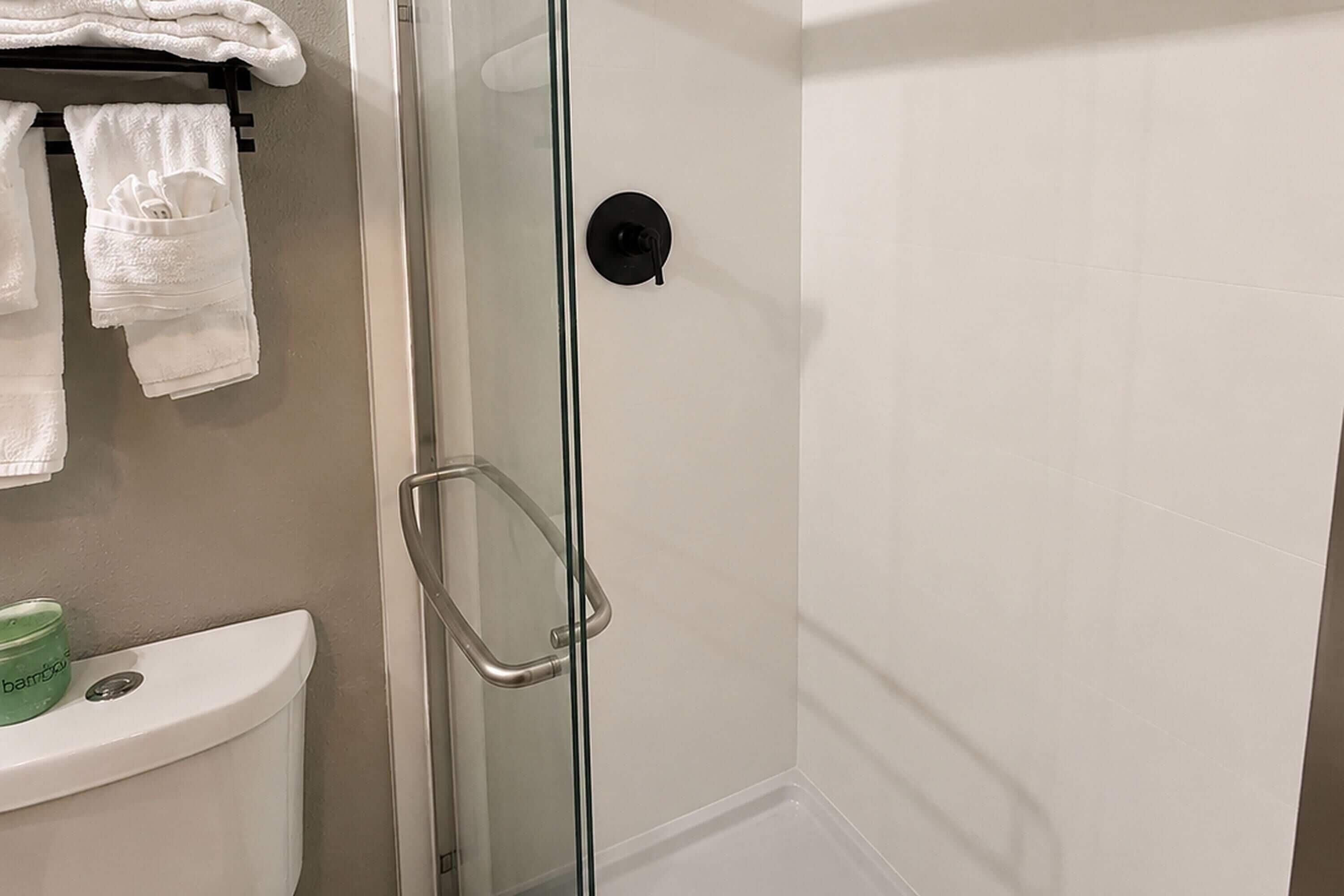 A bathroom with a glass shower enclosure, a toilet, and a towel rack with folded towels.