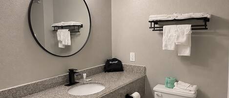 Un baño con un espejo redondo, un lavabo, un inodoro y toalleros.